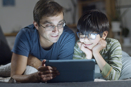 A father and his young son bonding while watching something on a tablet together in the evening.
